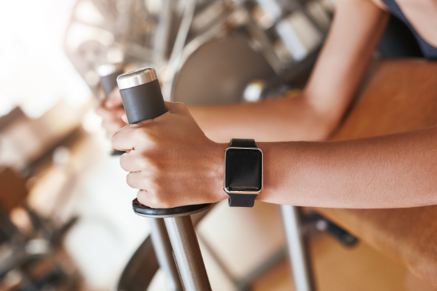 Close-up view of a person's hands gripping the handles of a stationary bike during a workout, wearing a fitness tracker on their wrist to monitor performance.