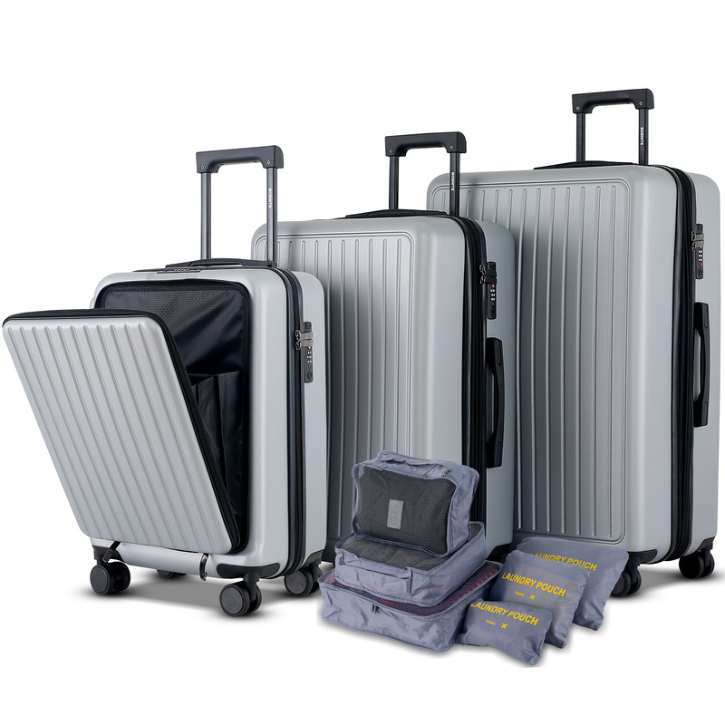 A set of silver hard-shell luggage in varying sizes, with telescopic handles extended. Next to them is a collection of grey packing pouches labelled for laundry.