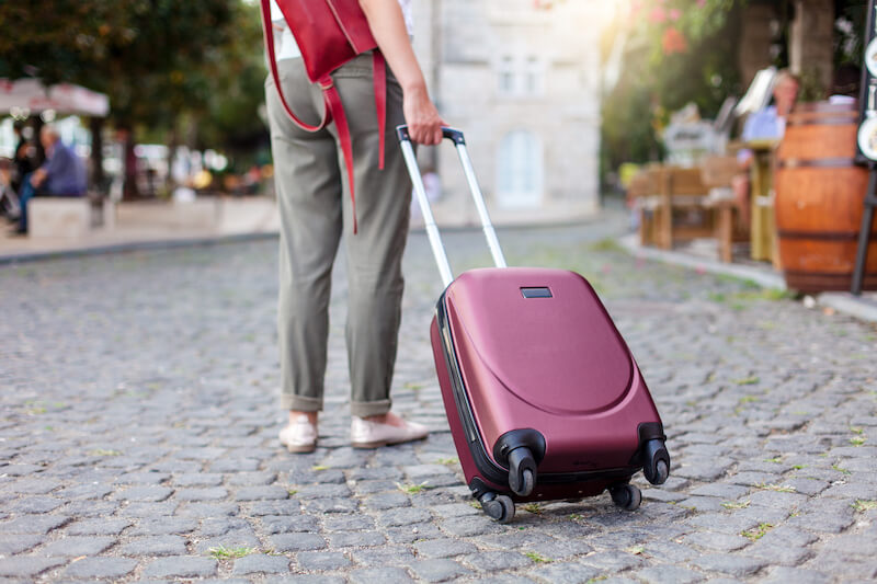 A person in a casual outfit pulls a sleek maroon rolling luggage