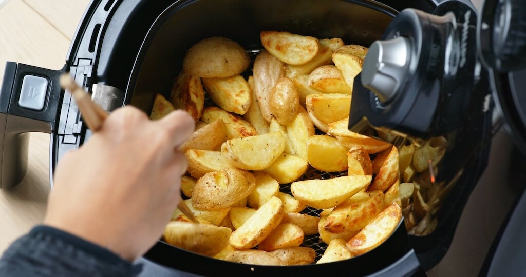 Person cooking golden potato wedges in an air fryer, demonstrating what can you cook in an air fryer.