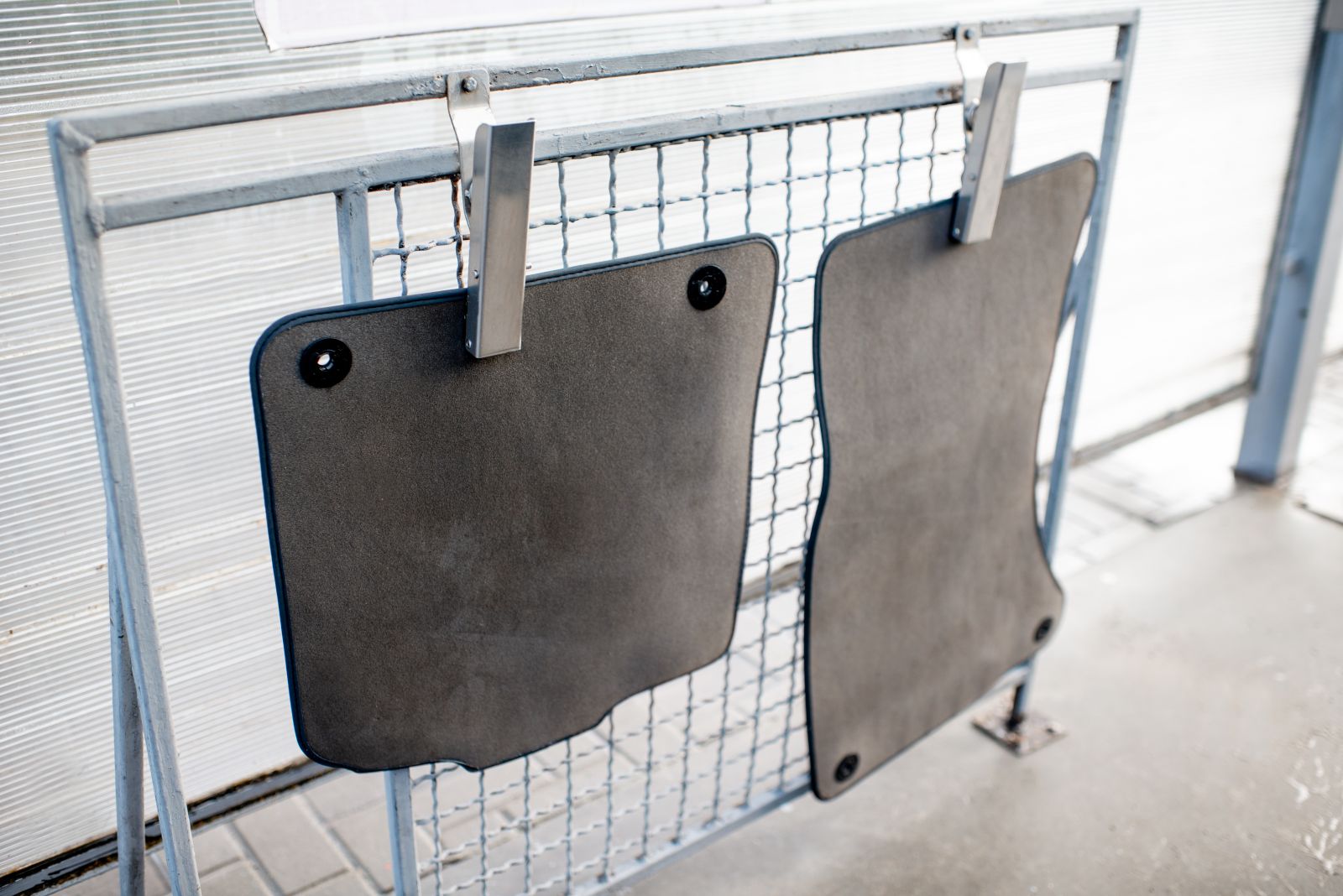 Two car floor mats hanging to dry on a metal rack after being washed. The final step in how to clean car floor mats is by drying them, which helps avoid mould.