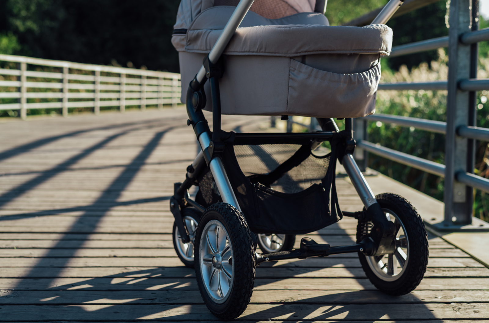 A baby stroller on a sunlit wooden boardwalk, emphasizing its sturdy wheels and comfortable design, ideal for outdoor use.